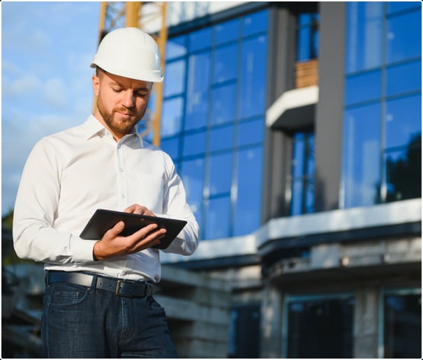 Bau-Experte mit ERP-Tablet vor Baustelle